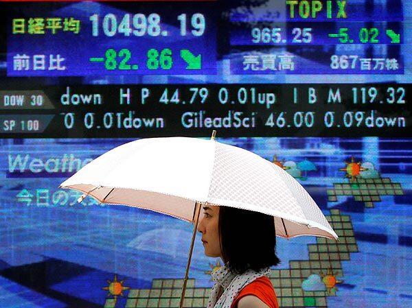 A woman walks in front of the electronic stock board of a securities firm in Tokyo. The benchmark Nikkei 225 stock average lost 82.86 points, to end Tuesday's morning session at 10498.19.