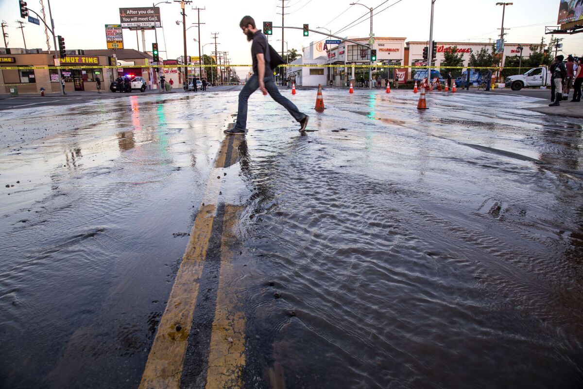 A pedestrian crosses flooded Santa Monica Boulevard at Highland Avenue, where a water main ruptured on Oct. 27, flooding the streets and slowing traffic.