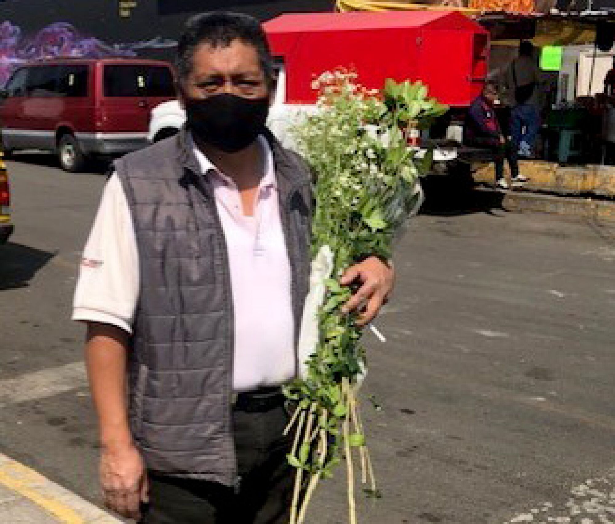 A man in a mask cradles a bouquet of flowers in his left arm