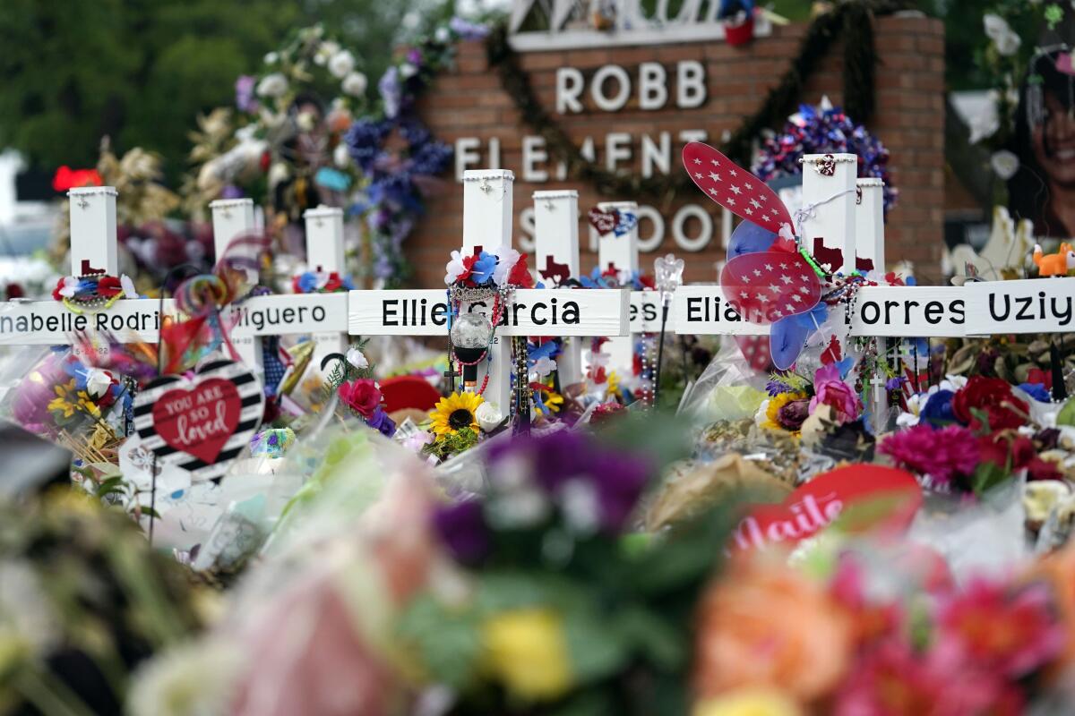 Crosses are surrounded by flowers and other items at a memorial outside a school