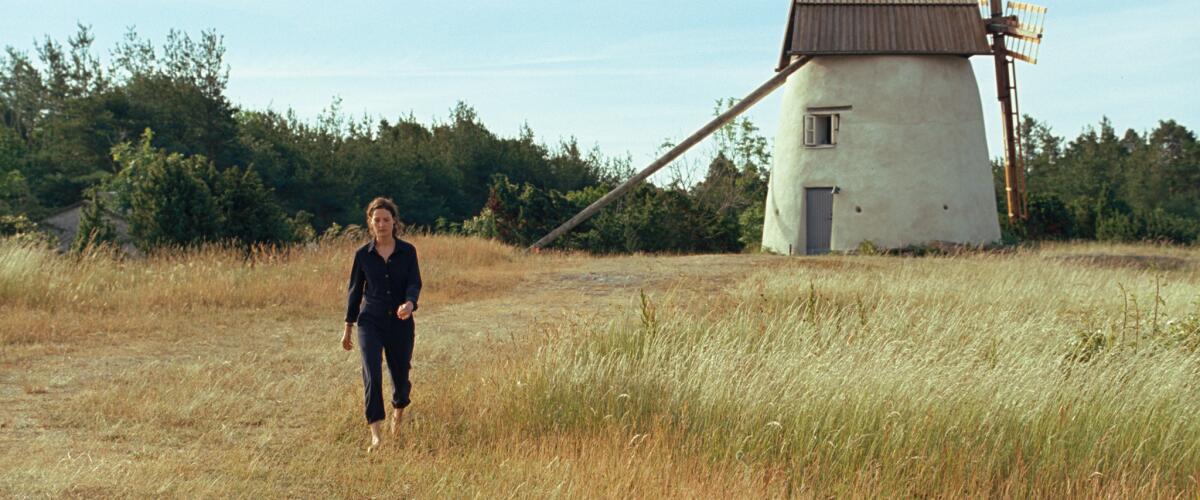 A woman walks through a field, with a windmill in the background, in the movie "Bergman Island."