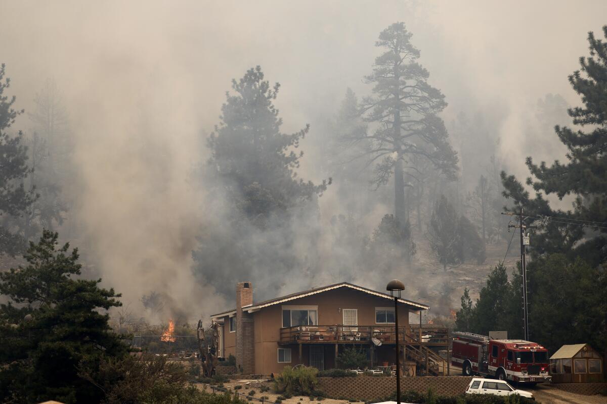 Wildfire smoke envelopes towering trees behind a home.