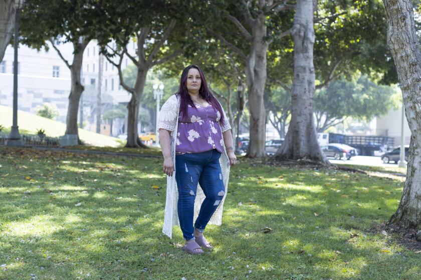 Sonja Verdugo stands on a grassy hill in the shade of several large trees