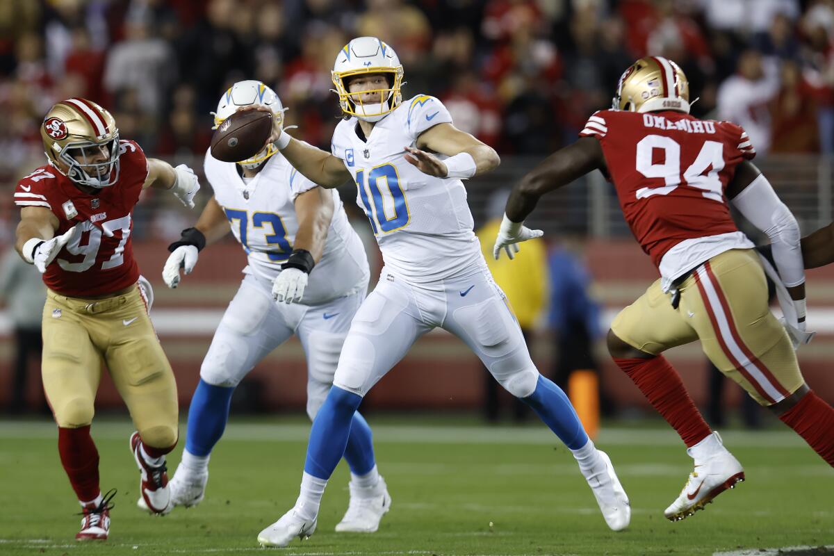 Chargers quarterback Justin Herbert (10) passes while pressured by 49ers  Charles Omenihu (94)  and Nick Bosa.