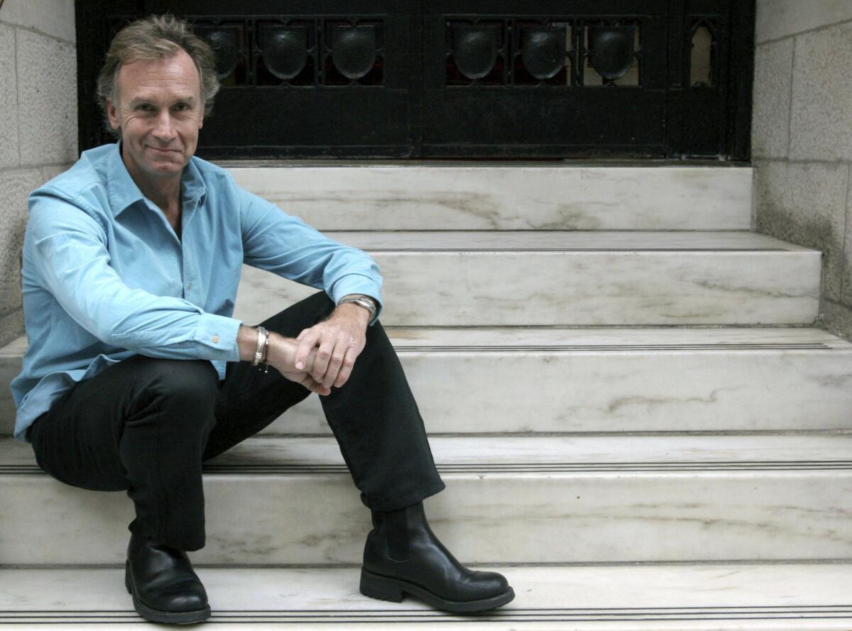 A man wearing a blue dress shirt and black pants sits on marble stairs