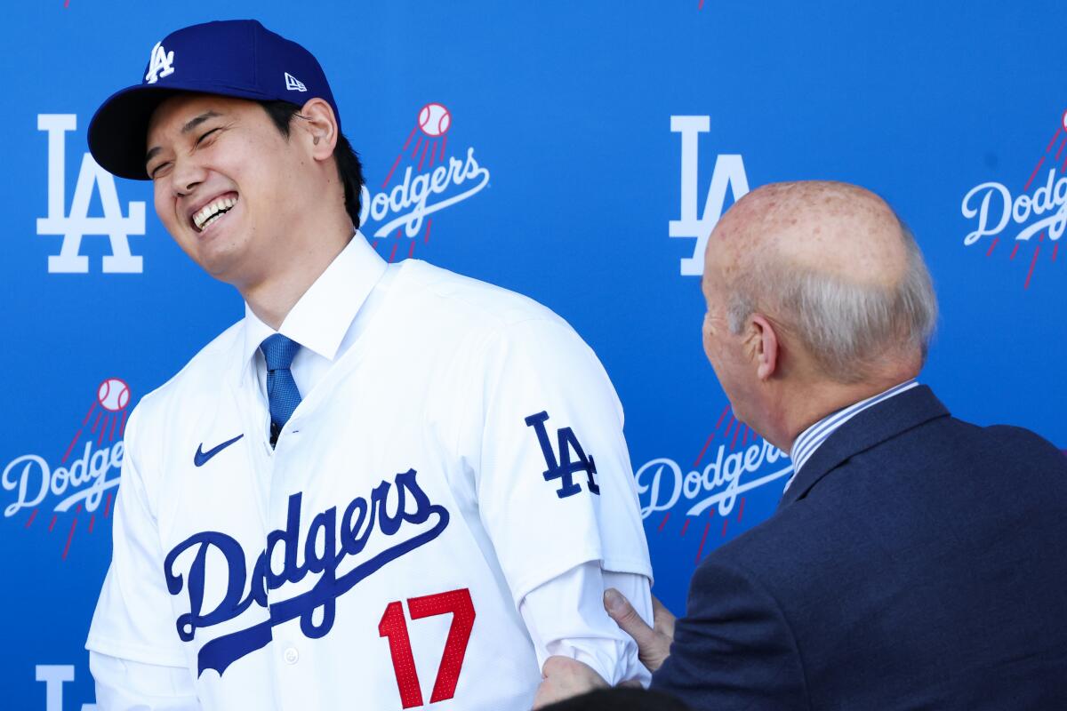 Shohei Ohtani in a Dodgers uniform shares a laugh with Dodgers President Stan Kasten at Dodger Stadium.