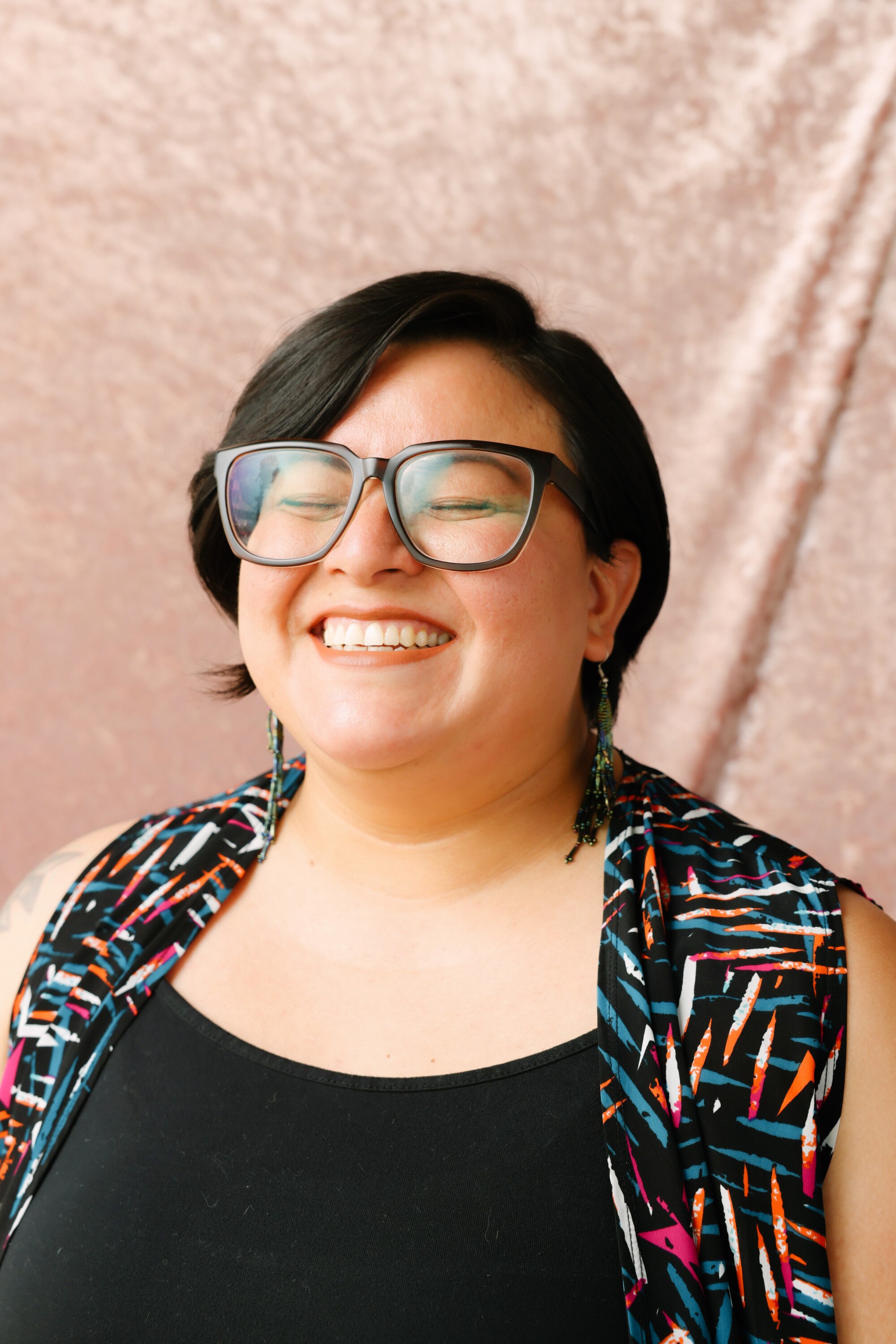 A person with black-framed eyeglasses closes their eyes and smiles.