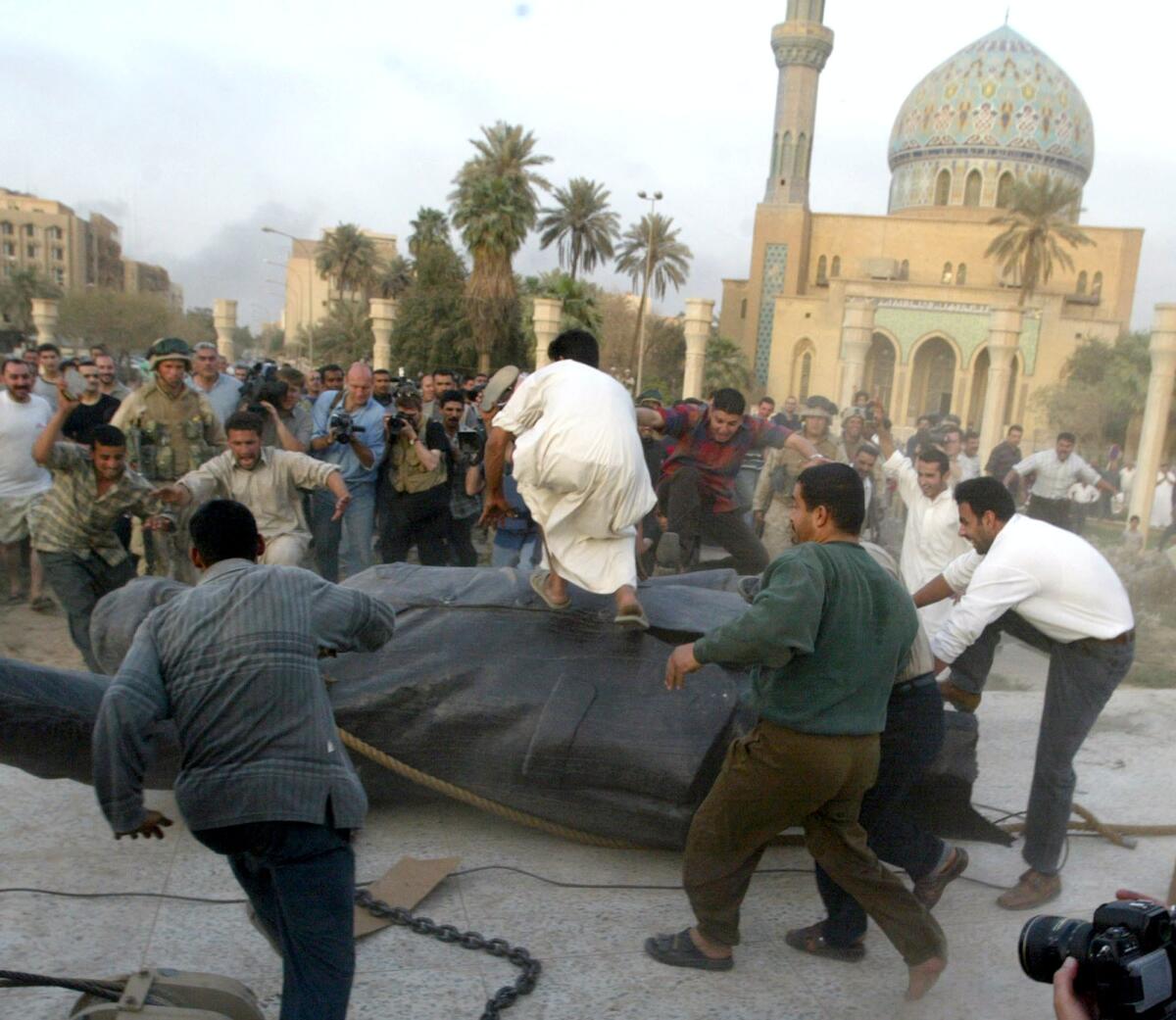 Iraqi civilians rush to the torn down statue of then Iraqi President Saddam Hussein in Bagdad on April 9, 2003.