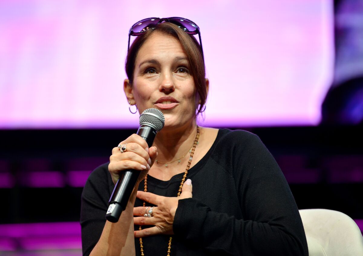 Amy Jo Johnson speaks into a microphone and holds one hand to her chest during a panel discussion