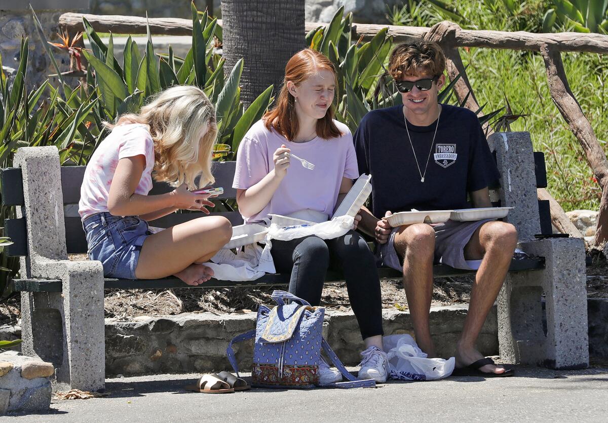 Three high school-aged kids have lunch at Heisler Park in Laguna Beach on Thursday.