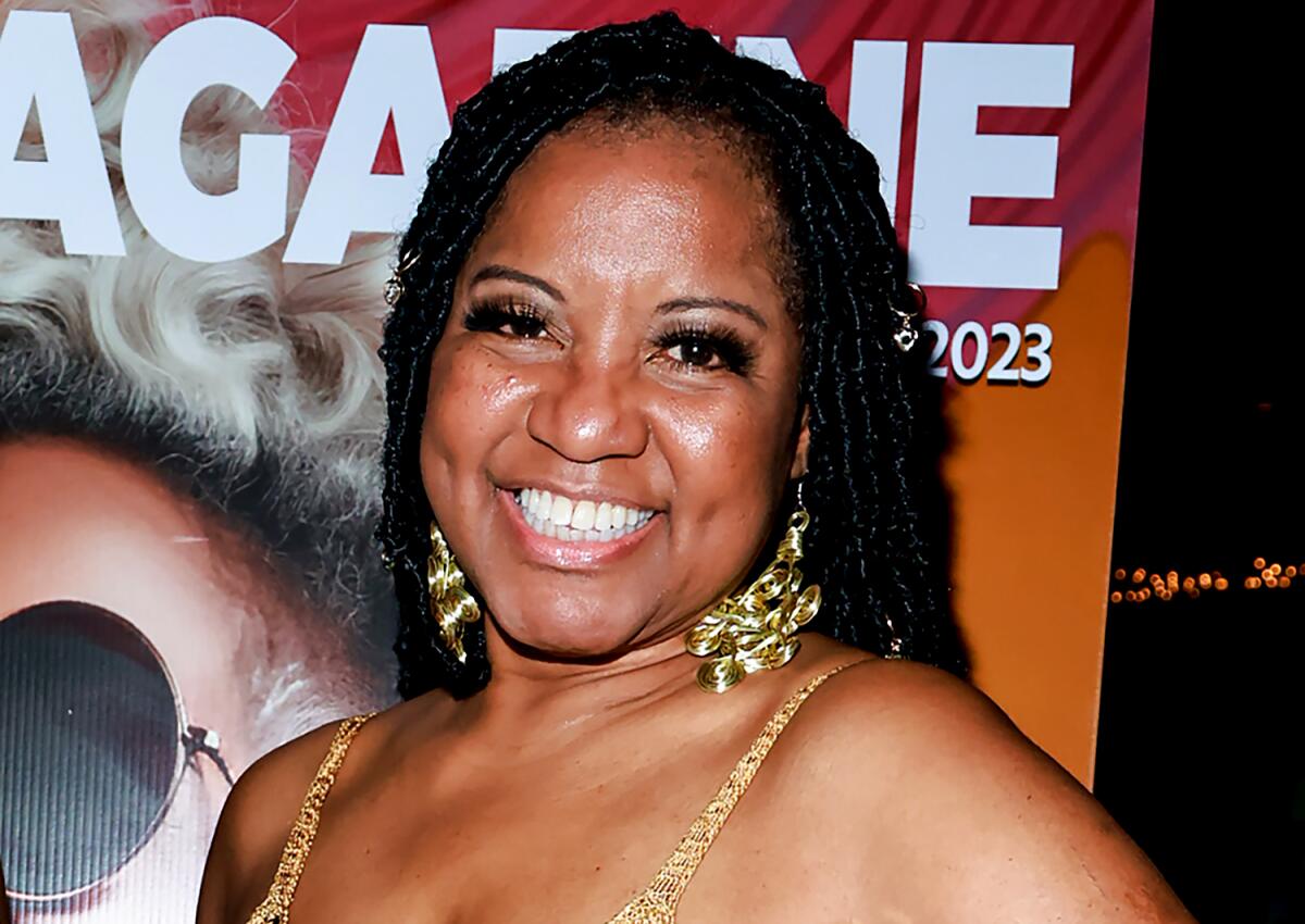 Yolanda Favors smiling wearing gold chunky earrings in front of a multicolored poster. 