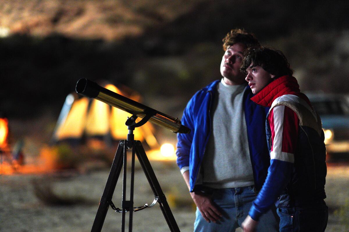 Two young men stand next to a telescope.