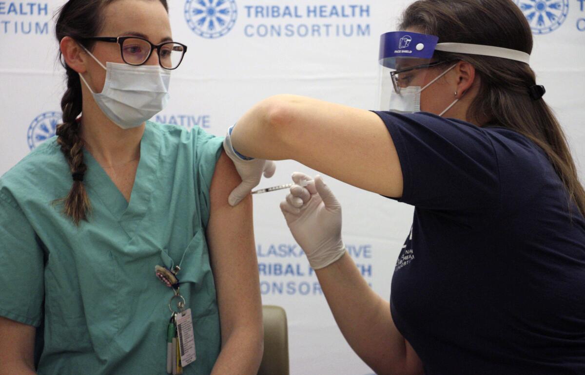 A woman in green scrubs has her left sleeve rolled up for a vaccine shot