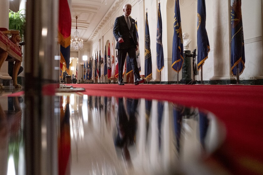President Biden walks on a red carpet between rows of state flags in a White House hallway