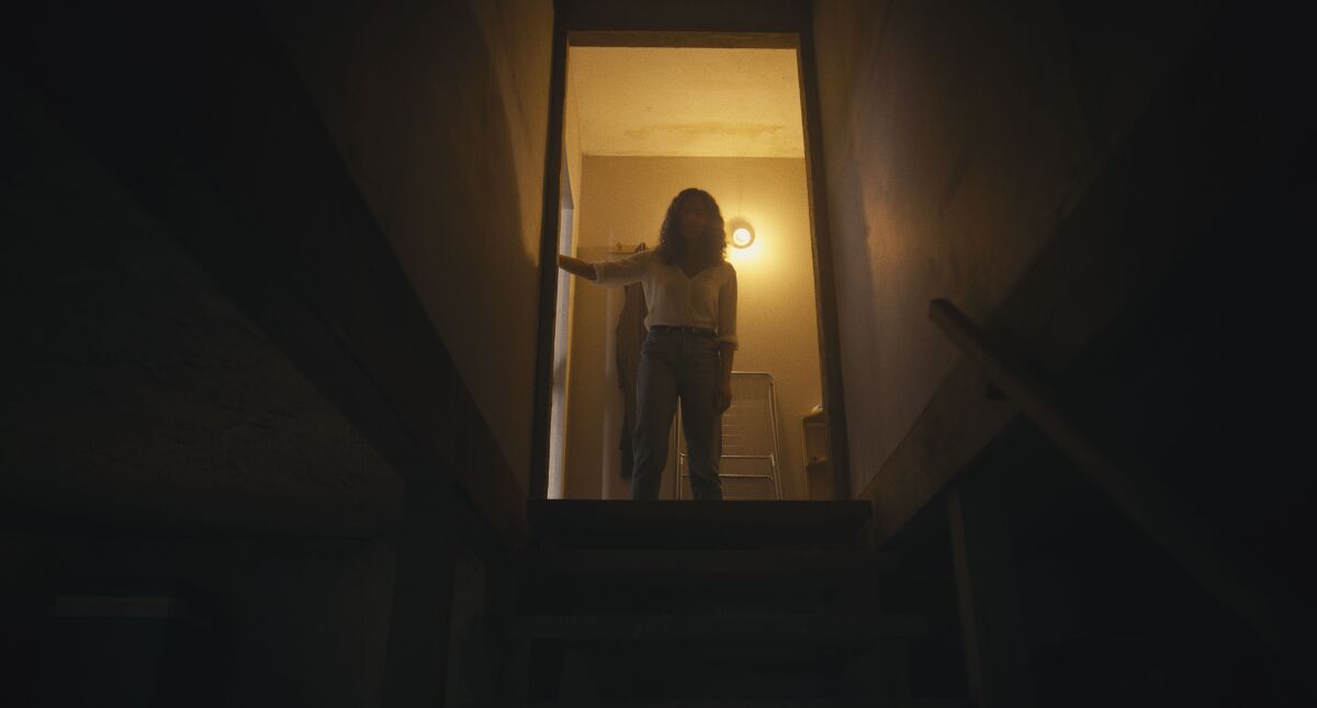 A woman holds a flashlight up the stairs.