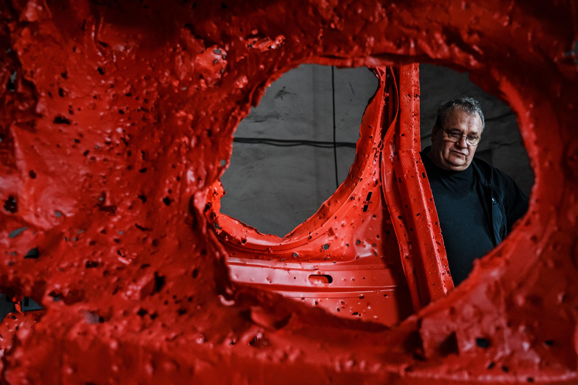 A man looks through a twisted red sculpture fashioned from a destroyed Russian military vehicle. 
