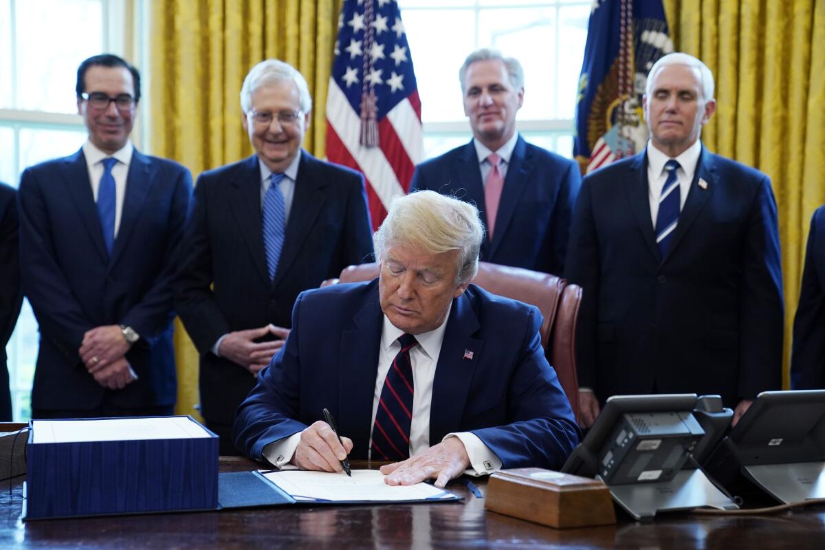 President Trump signs a bill on his desk as a row of advisors and lawmakers stand behind him