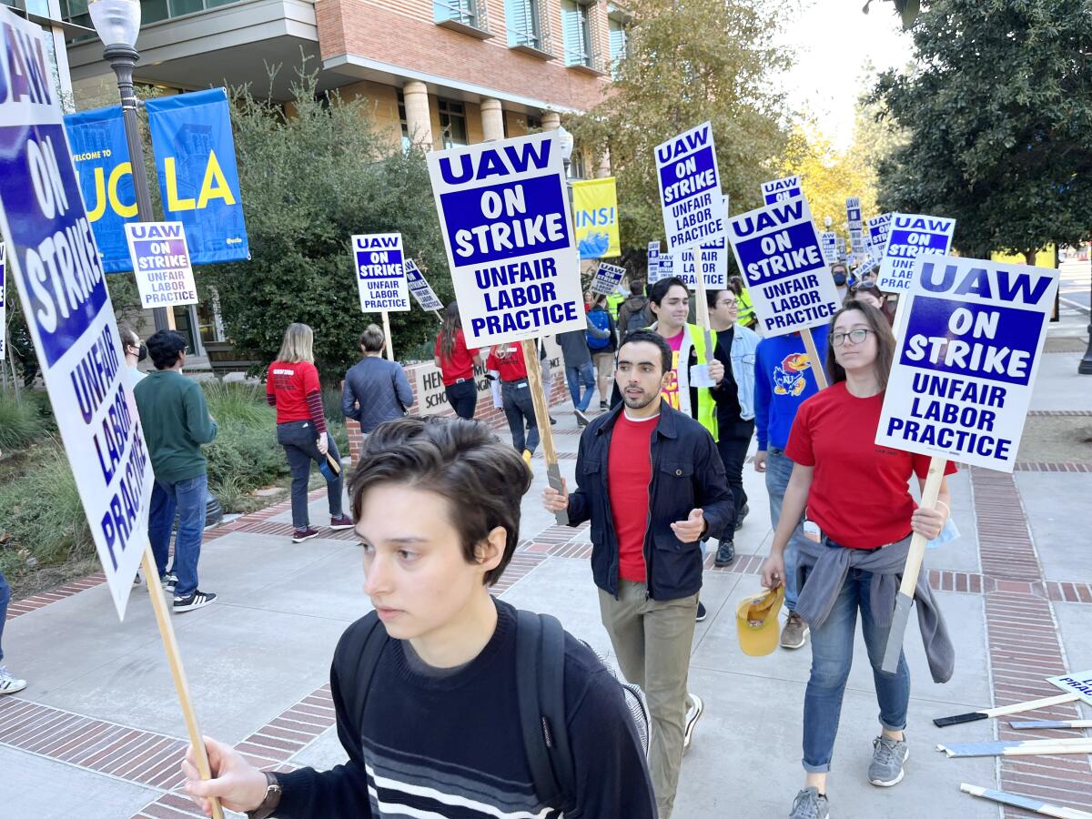 People walk and hold signs saying "UAW on Strike. Unfair Labor Practice."