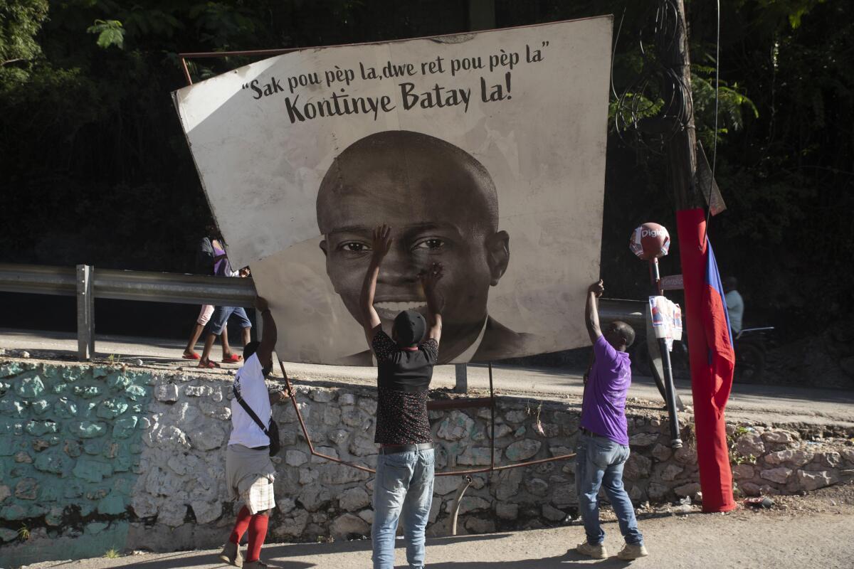 Supporters of slain Haitian President Jovenel Moise hold a sign with his picture.