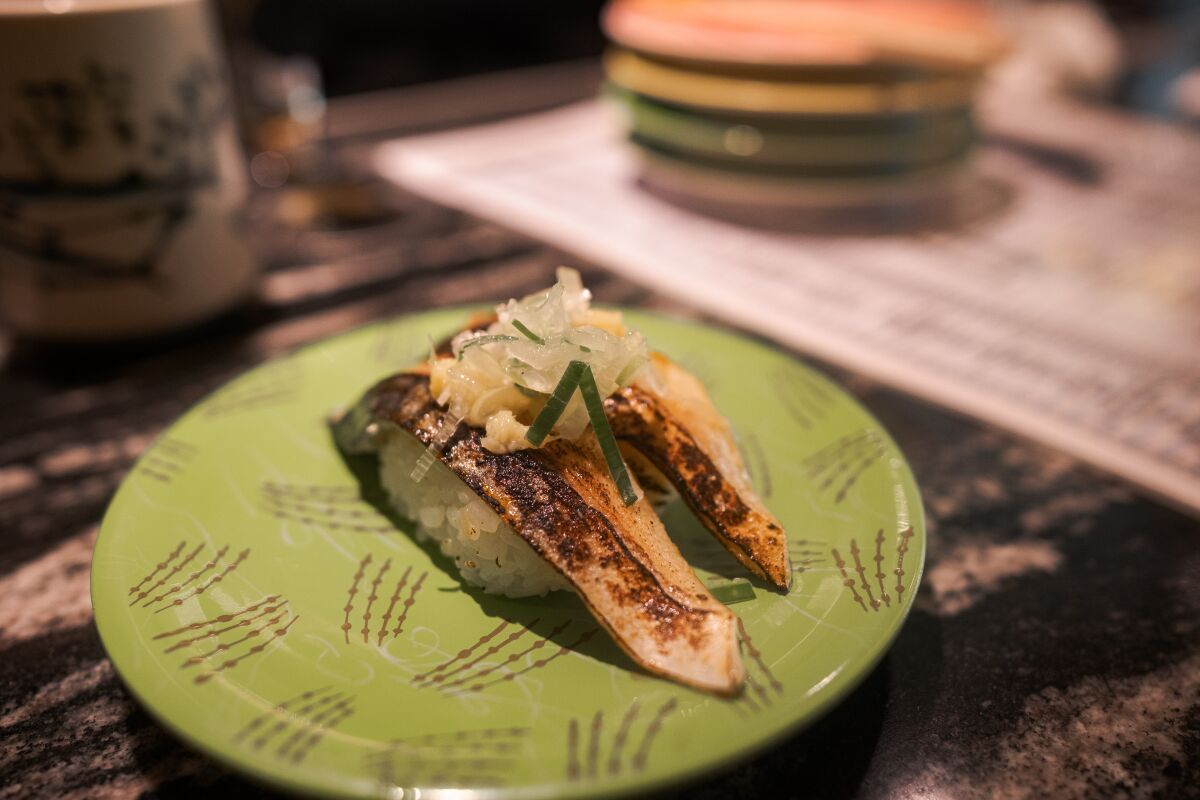 A plate of broiled mackerel nigiri sushi with horseradish and onion at Hanamaru Ginza, a conveyor belt sushi restaurant in Japan.