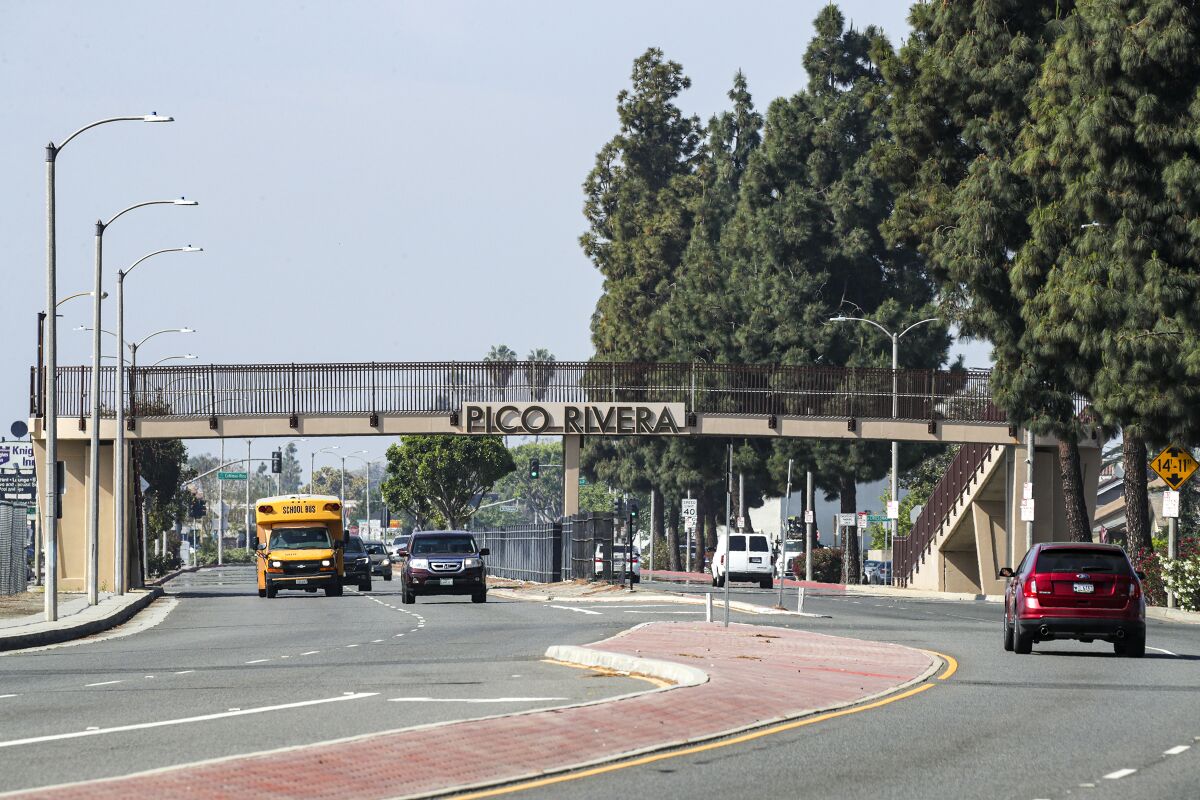 A road with a pedestrian bridge with the words "Pico Rivera" on it.