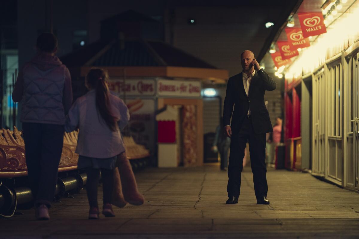 An imposing man in a suit takes a phone call as a woman and her daughter walk by