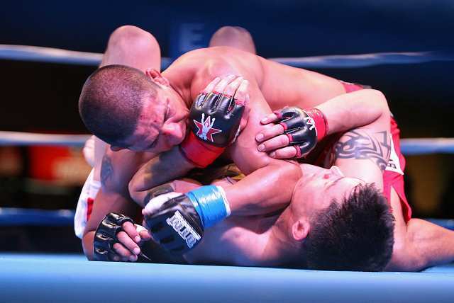 Huntington Beach's Carlos Garces, left, has Isaac Gutierrez on the canvas as they mix it up during Fight Club OC in the Hangar at the Orange County Fair and Event Center.