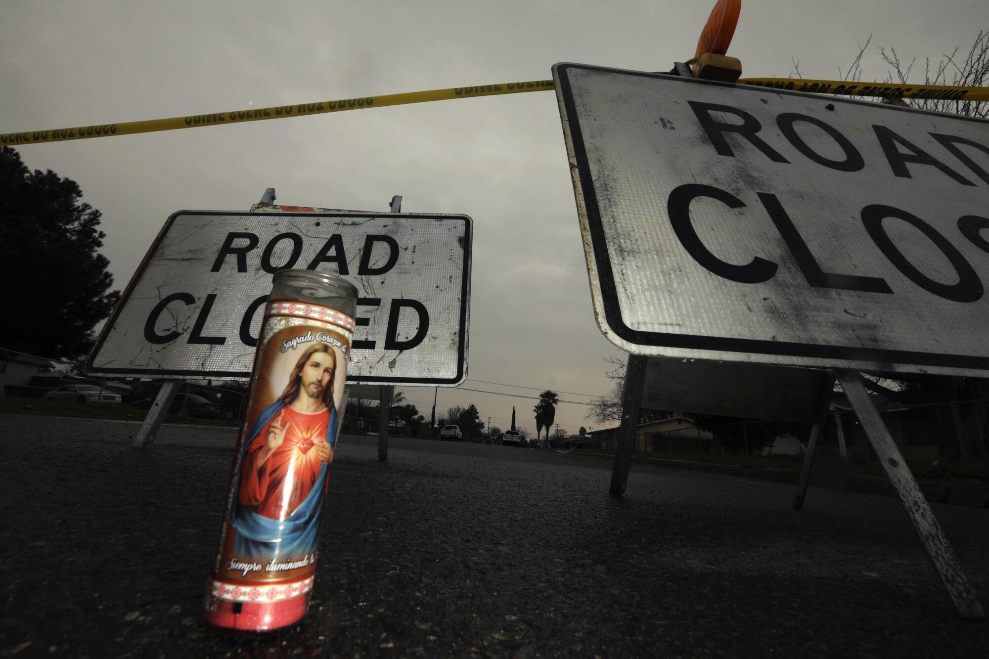 A votive candle on asphalt near "Road Closed" signs topped with yellow police tape