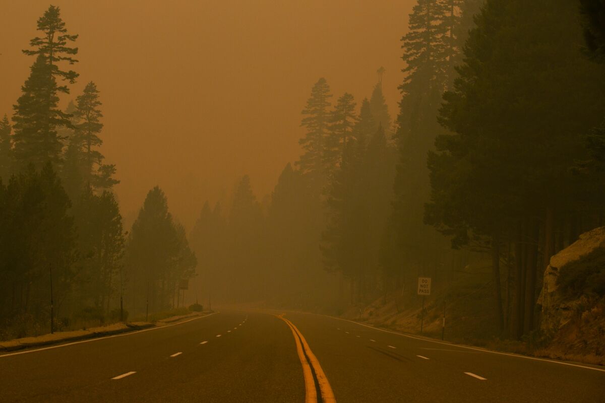 Orange sky and thick smoke are seen above an empty highway.