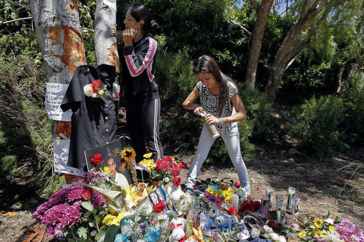Bernice Torres, left, carves a heart in a tree Monday as Nicole Balbuena, right, lights a candle at a memorial where Luis Adrian Torres died in a car crash on Sunday.
