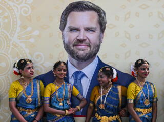 Dancers wearing traditional Indian attire stand in front of a poster depicting U.S. Vice President JD Vance.