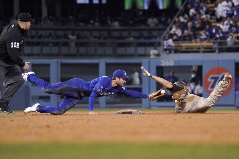 San Diego Padres' Eric Hosmer, right, slides in for a double as Los Angeles Dodgers second baseman Trea Turner, center, attempts to tag him while second base umpire Jeremy Riggs watches during the seventh inning of a baseball game Tuesday, Sept. 28, 2021, in Los Angeles. (AP Photo/Mark J. Terrill)