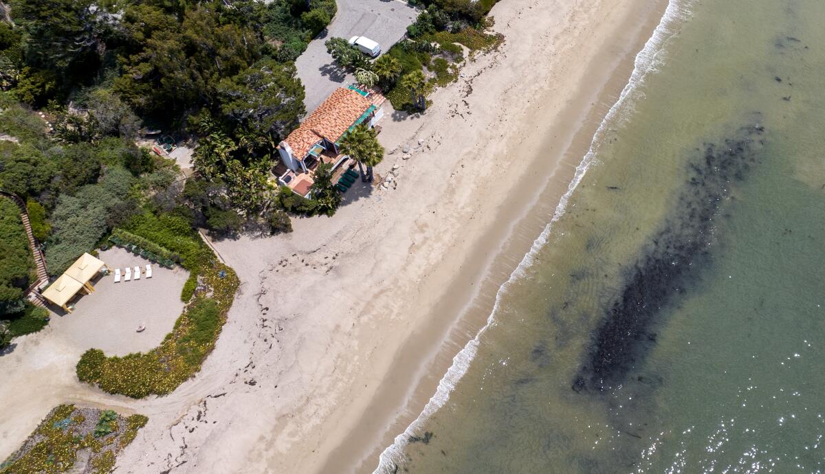 An aerial top-down frame of a beach diagonally cutting through the image with greenery and houses at left  