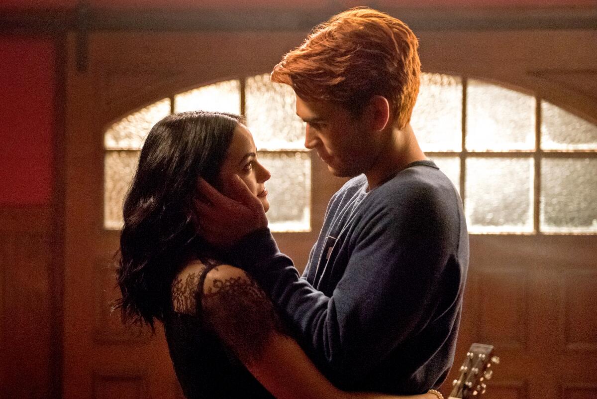 Camila Mendes and KJ Apa embrace as he caresses her face in a scene from "Riverdale."