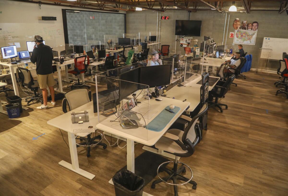 Office workers standing and sitting at desks in an office, distanced for COVID safety.