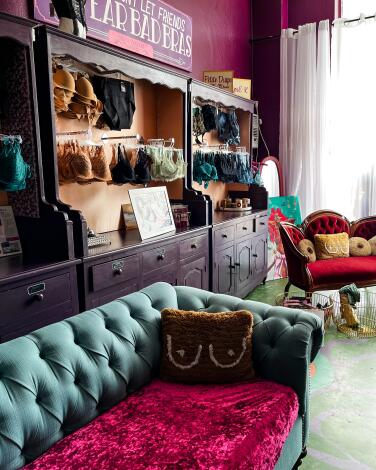 Bras hang in an armoire behind a suede green couch and red loveseat