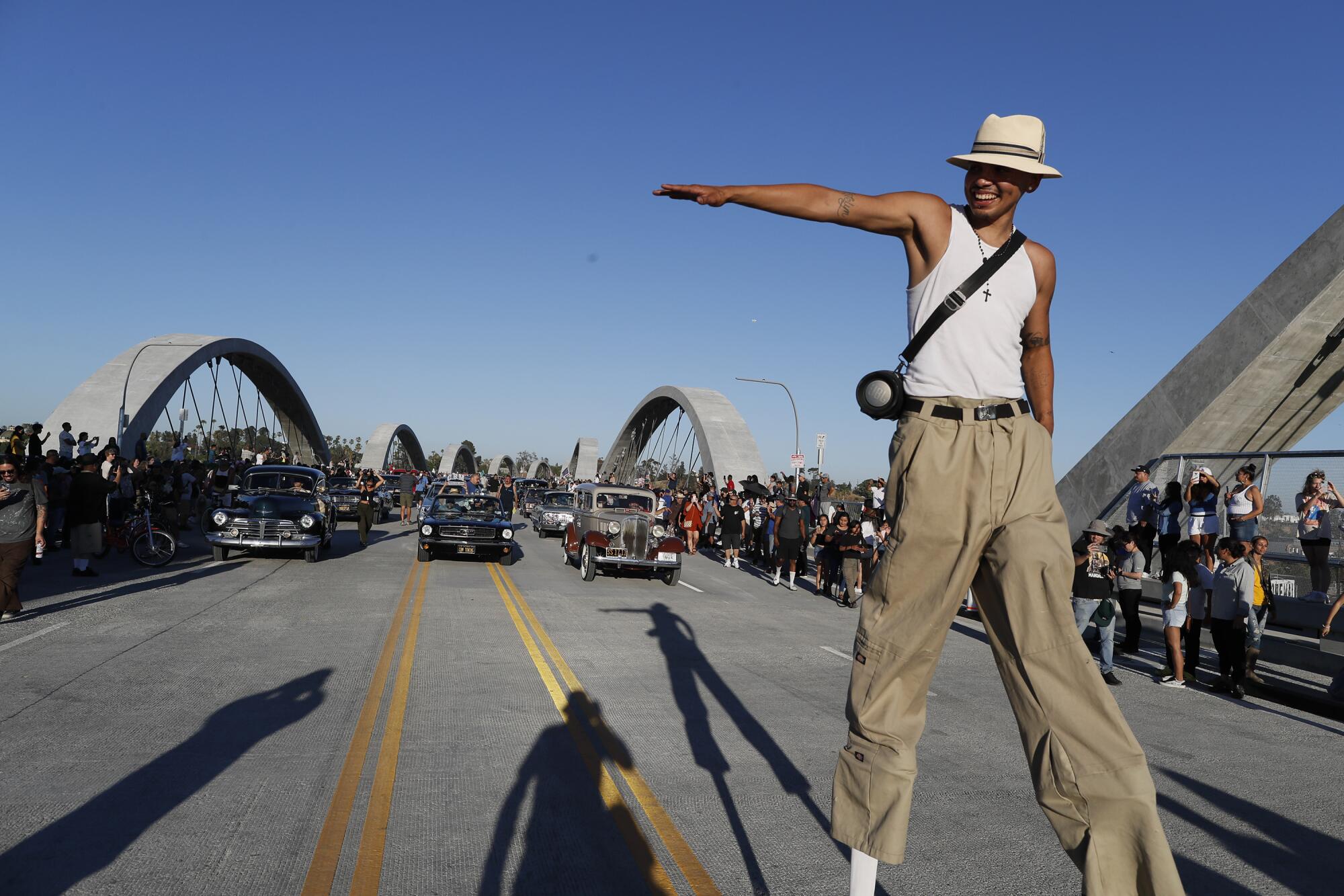 A man on stilts is shown with a group of lowriders on the 6th Street Viaduct.