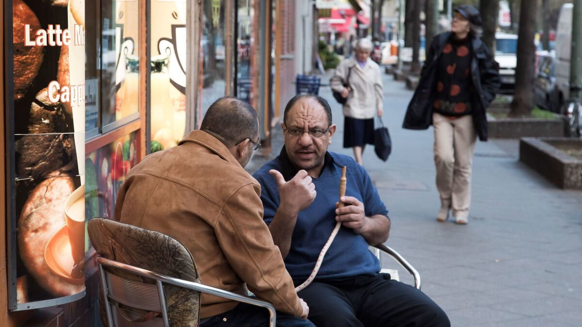 El Mohamed, right, smokes a hookah pipe as he talks with native Palestinian Yaser A Rabah in front of a bar at Sonnenallee in the Neukoelln district of Berlin.