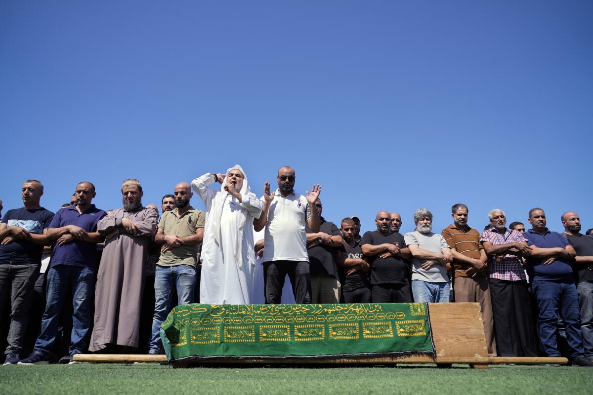 Mourners pray over a coffin covered in a green cloth with yellow designs.