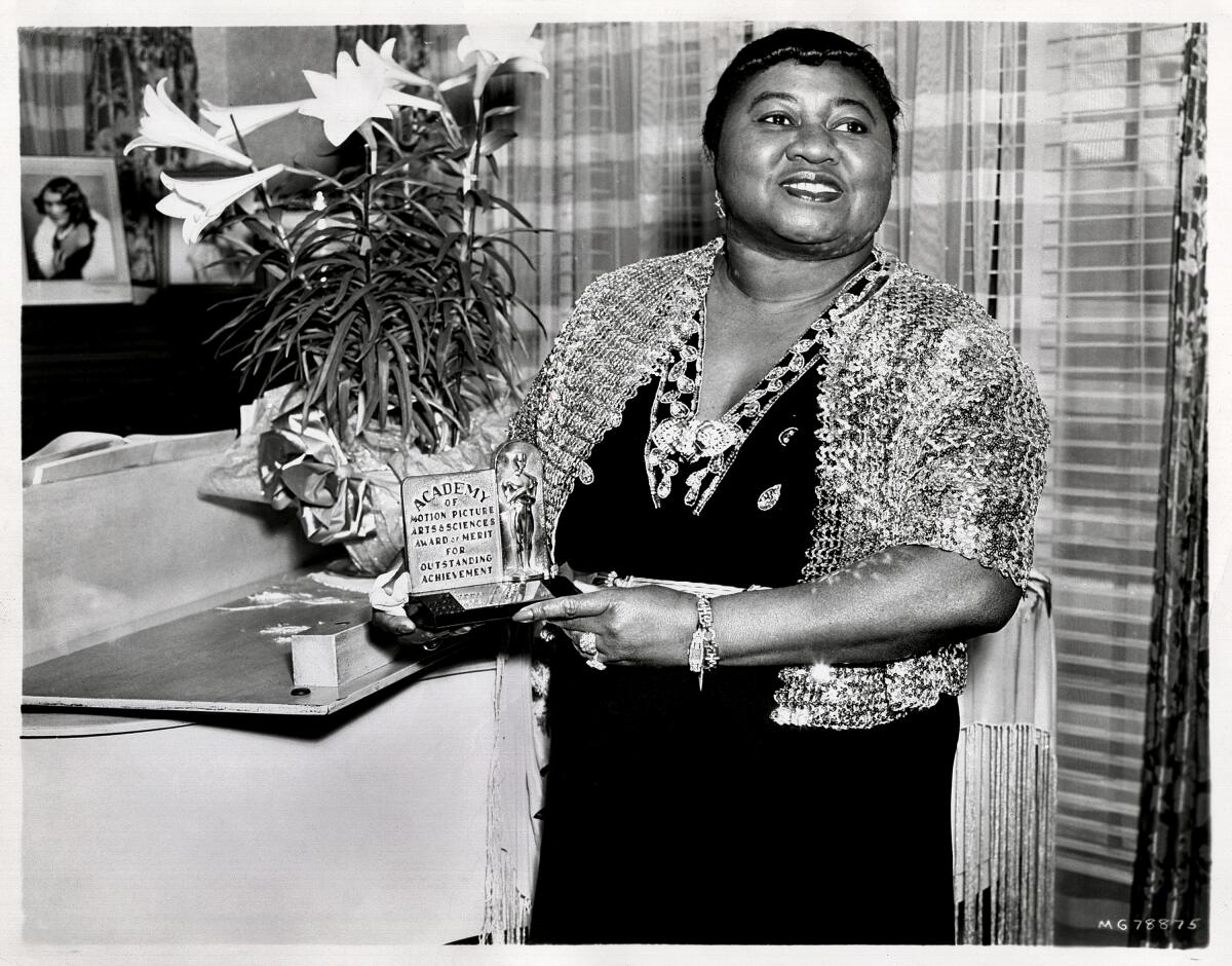 Hattie McDaniel stands next to white lilies and holds her Academy Award.