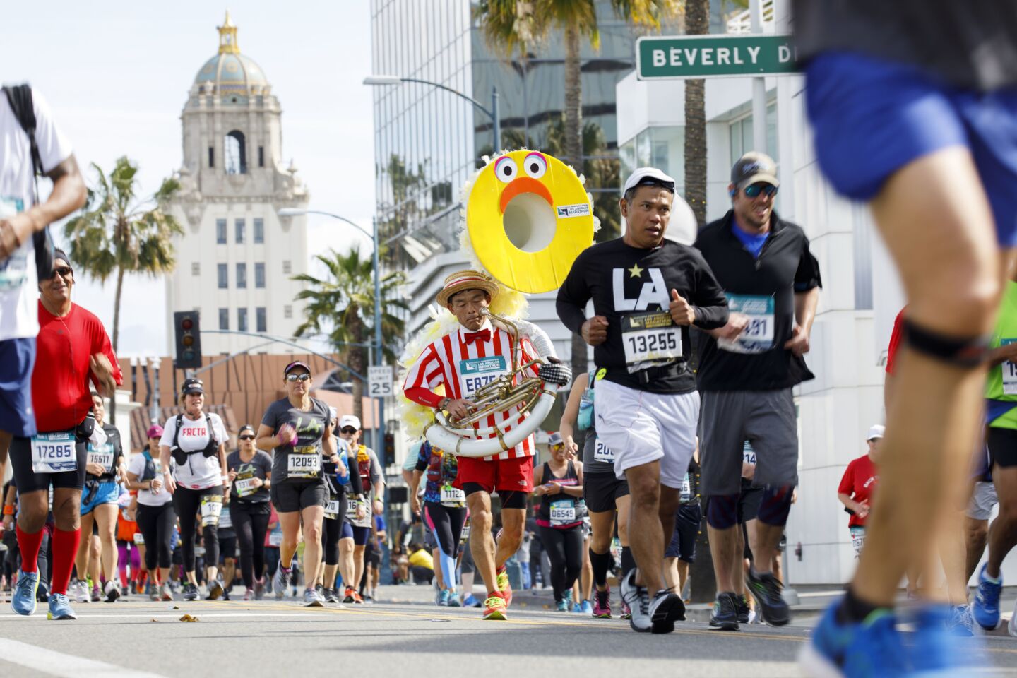 A runner carrying a tuba makes his way down Santa Monica Blvd at mile 17 of the L.A. Marathon in Beverly Hills.