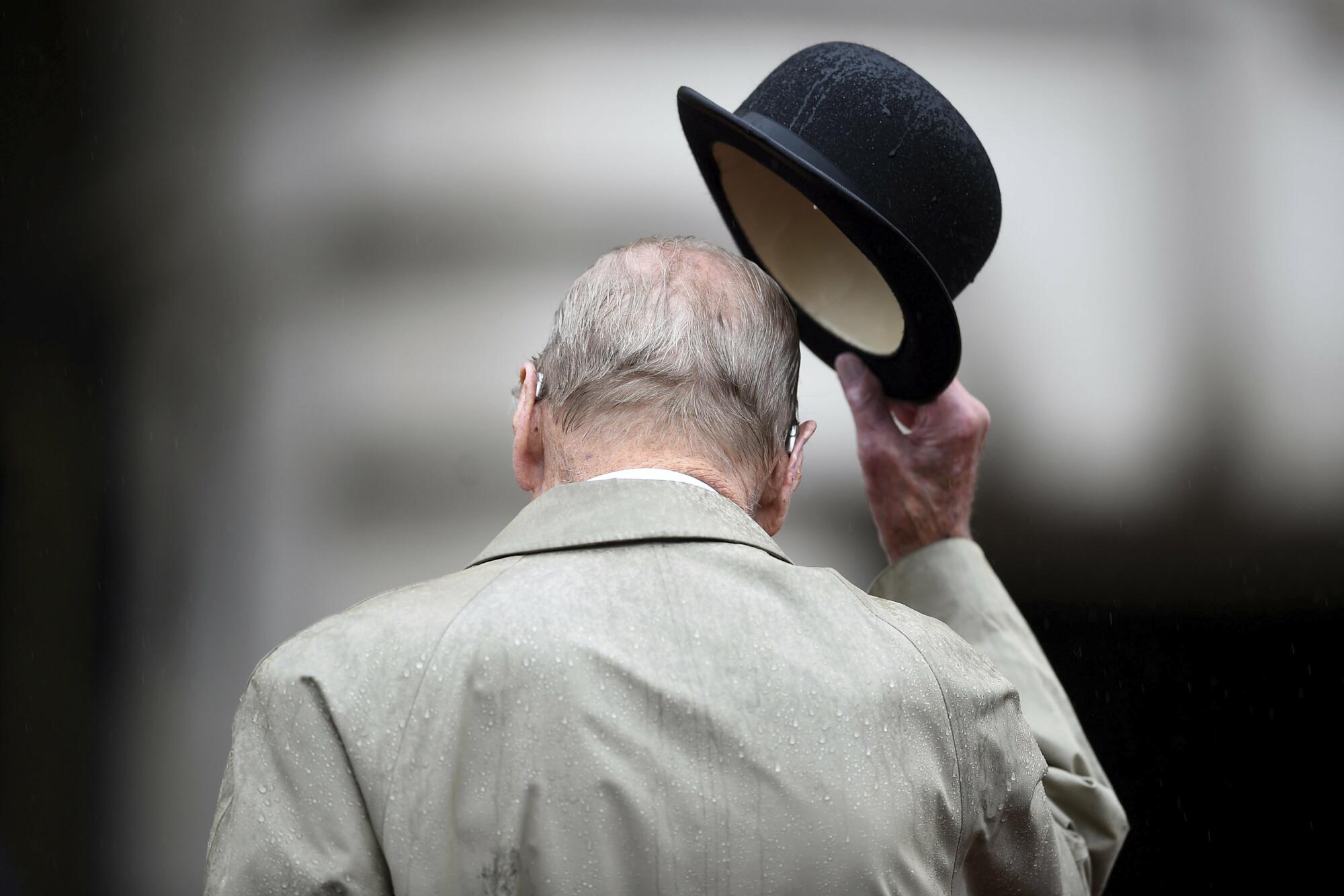 Prince Philip walks away lifting his hat.