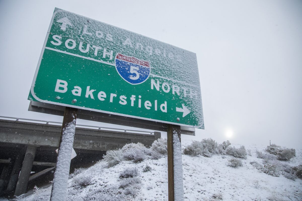 Snow on a freeway sign and a hillside next to an overpass