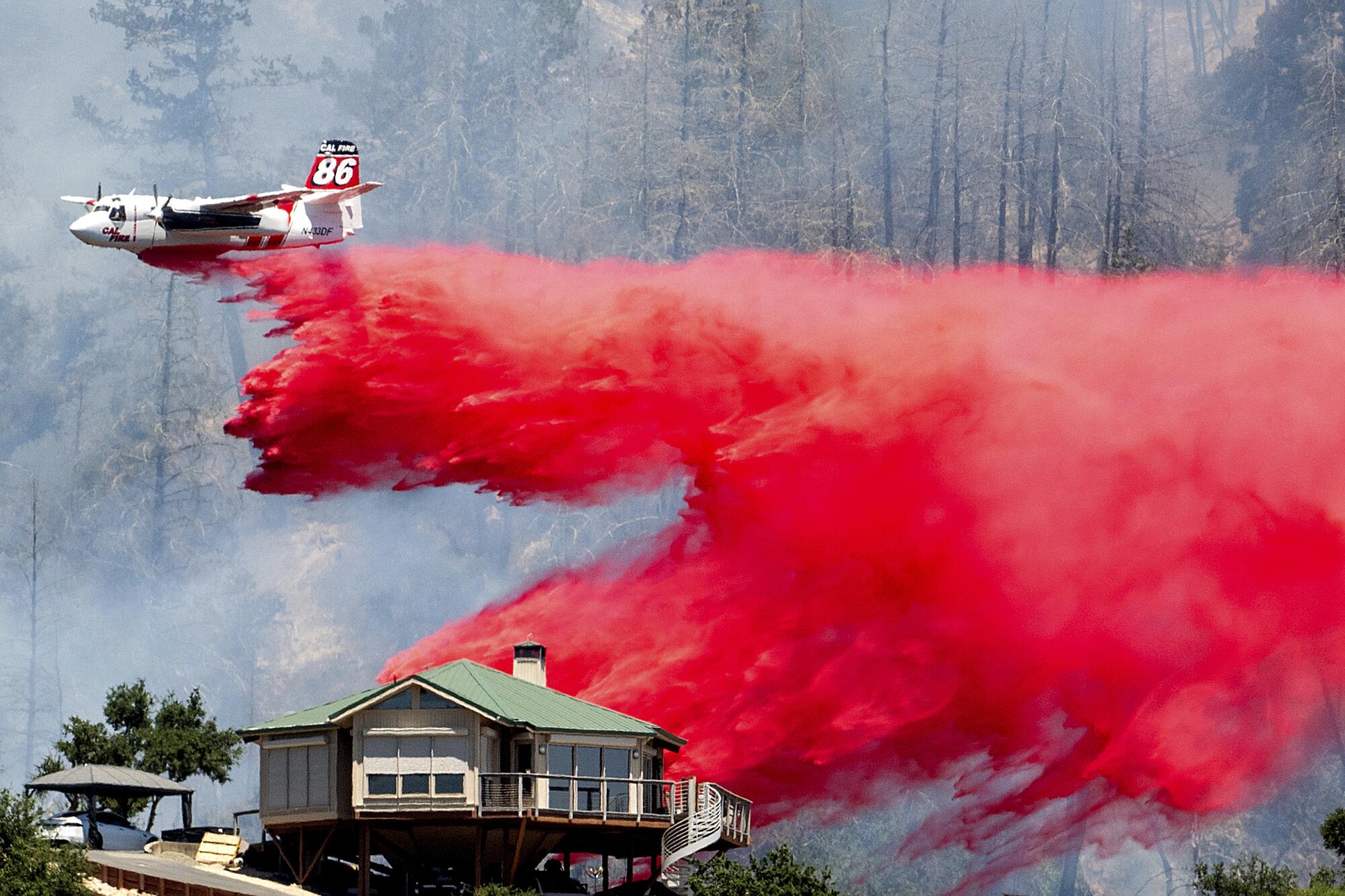 An air tanker drops pink fire retardant behind a home during a wildfire. 