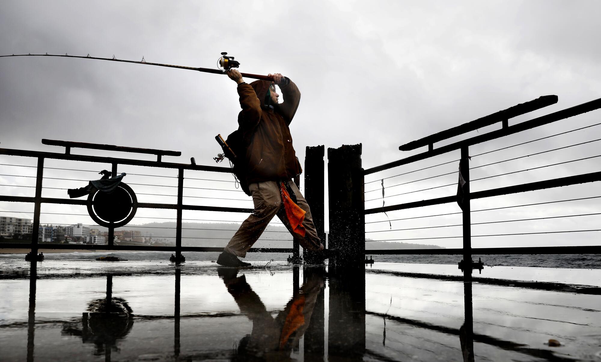 A man fishes in the rain on a pier.