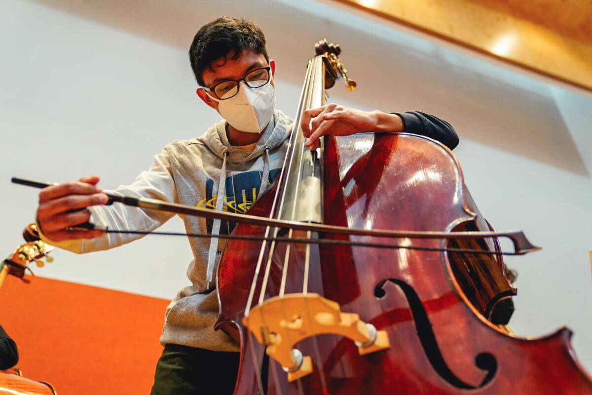 A teenager plays a string bass with a bow. 