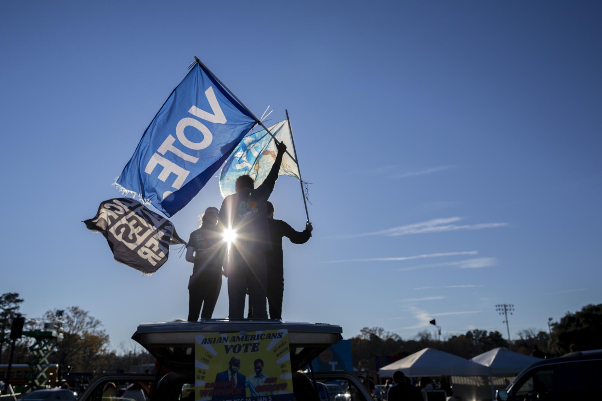 Sunshine casts three people in silhouette, illuminating flags they're waving that say "Vote" and "Black Lives Matter." 