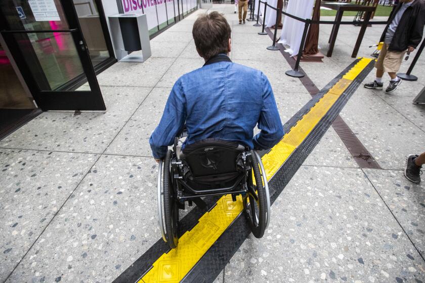 LOS ANGELES, CALIF. -- THURSDAY, SEPTEMBER 26, 2019: Television writer David Radcliff navigates his wheelchair over an electric cable channel at The Bloc shopping complex after rolling out of Metro’s 7th Street Station in Los Angeles, Calif., on Sept. 26, 2019. (Brian van der Brug / Los Angeles Times)