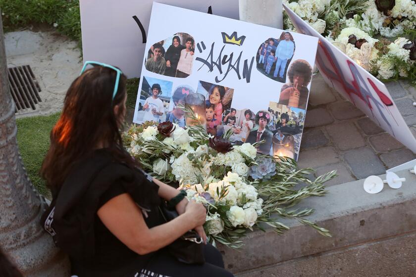 A woman prays next to a shrine for 15-year-old Aayan Randhawa, who went missing while swimming in the ocean off the shores of Huntington Beach on Sunday. The candlelight vigil, held at the Pier Plaza drew over a hundred family and friends who then walked to the end of the pier to throw flowers.