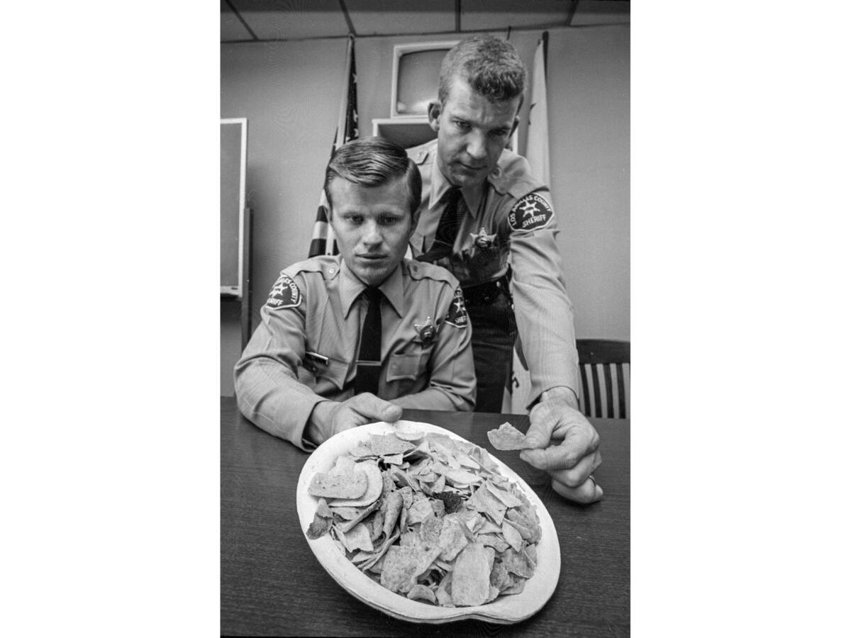 Two Los Angeles County sheriff's deputies hold a paper plate of potato chips and corn chips